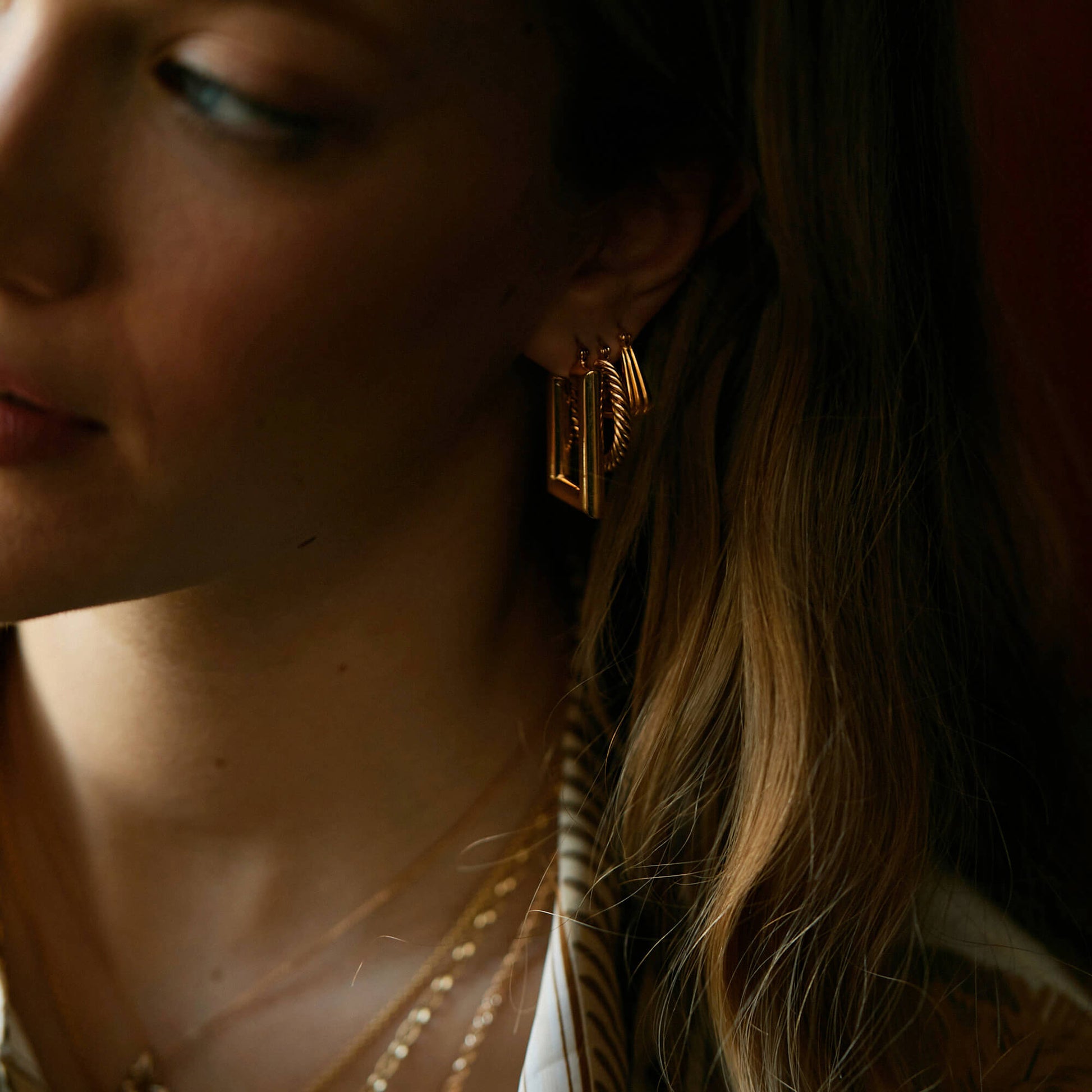 Model wearing Pawnshop signature gold hoops in earlobe- three siingles including rectangle, twist and ridge hoop earrings.